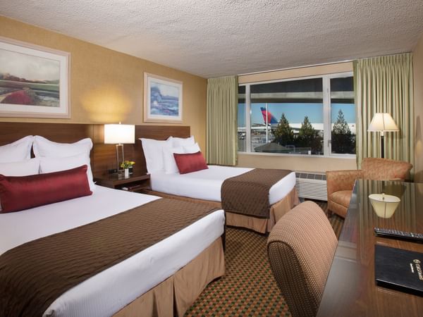 Two beds and desk in hotel room with view of airport