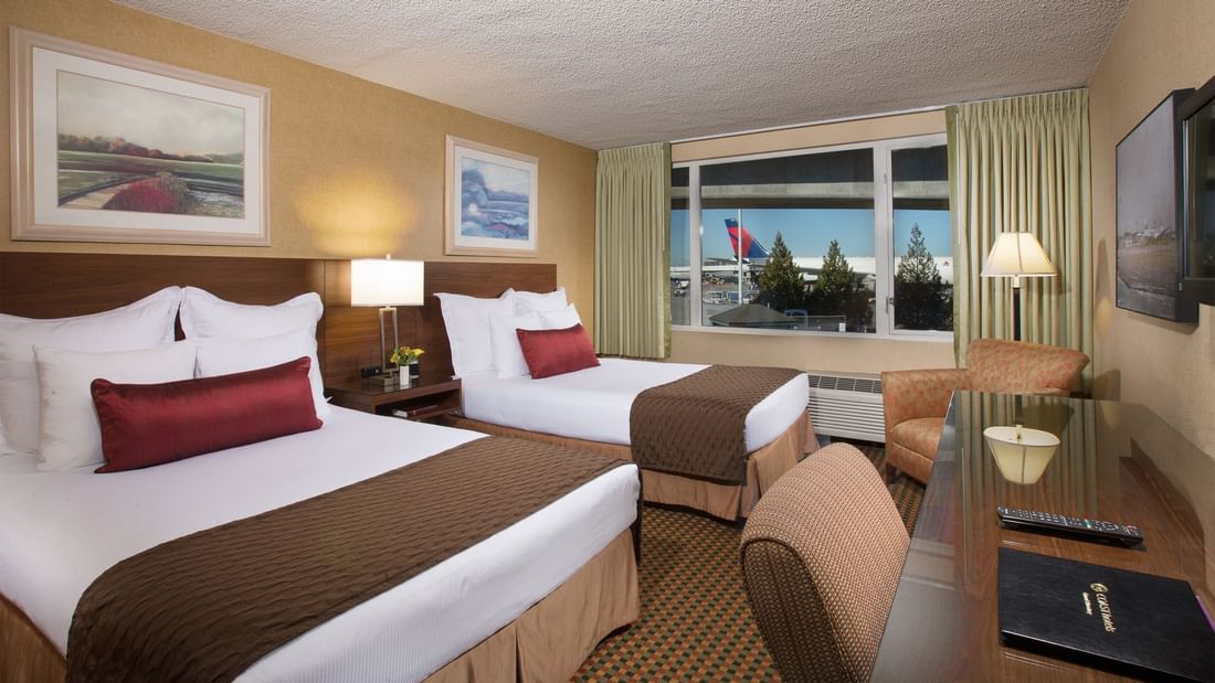 Two beds and desk in hotel room with view of airport