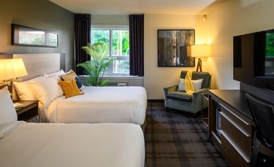 Two beds by a green armchair under a wooden frame, with a plaid carpet in Executive Two Queen View at Rodd Miramichi River