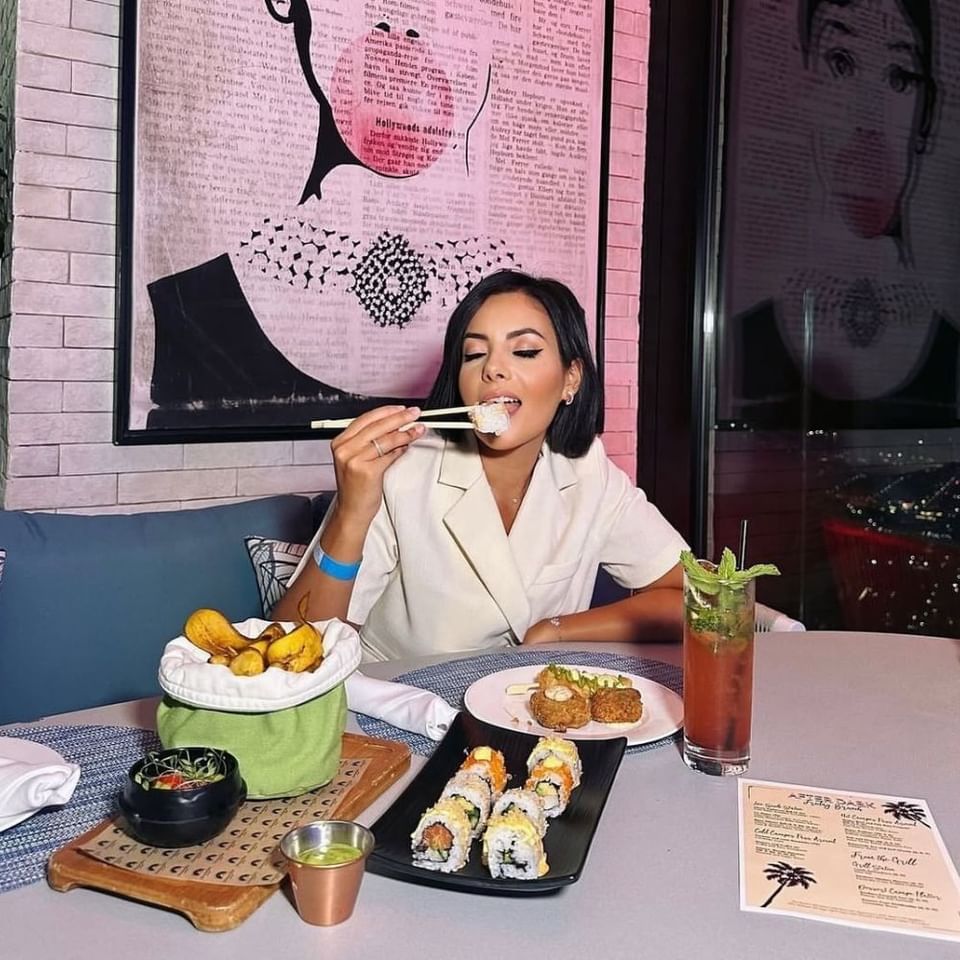 Woman eating sushi with chopsticks at the Indoor Lounge dining table with an After Dark menu at Malibu Sky Lounge & Bar