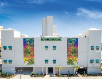 Bright white exterior of Margaritaville Resort Biloxi, showcasing vibrant palm tree murals and modern architecture