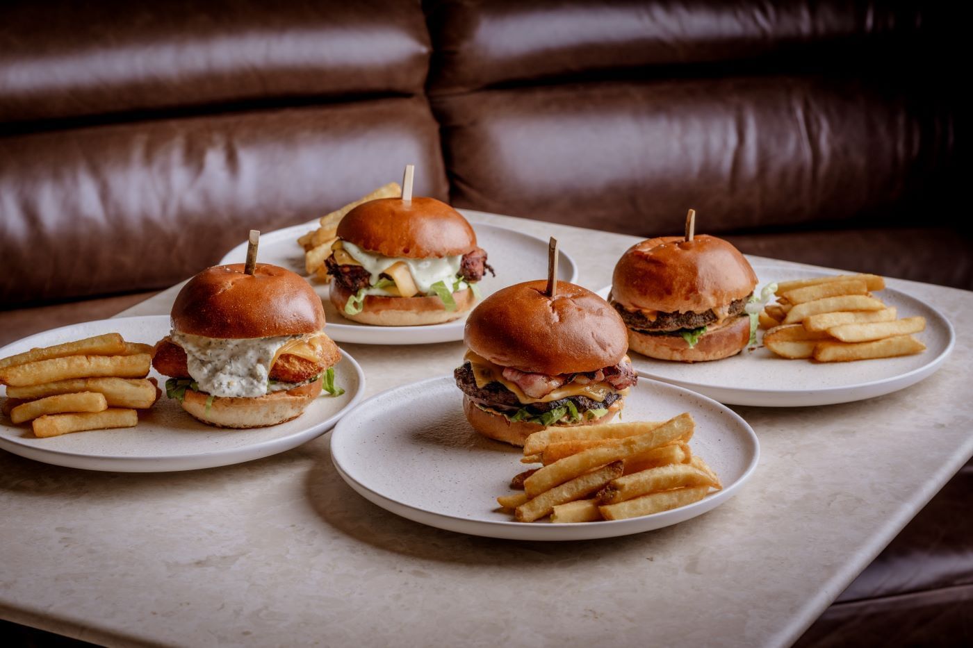 A range of Four burgers with fries on plates from the house classics section of the by day menu from The May Fair Bar.