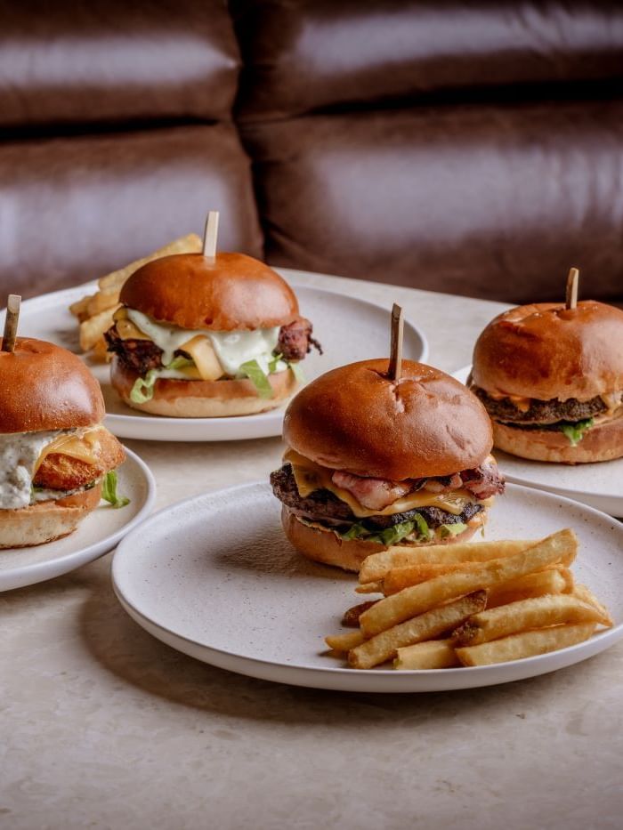 A range of Four burgers with fries on plates from the house classics section of the by day menu from The May Fair Bar.
