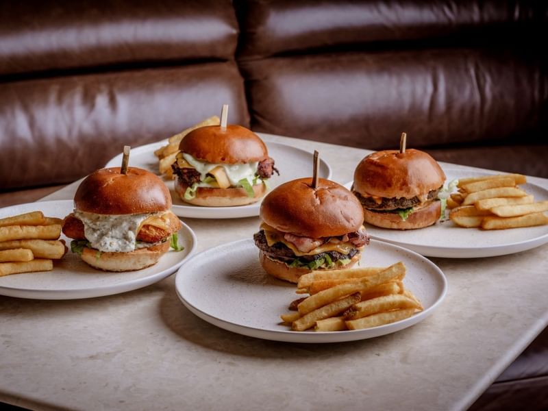 A range of Four burgers with fries on plates from the house classics section of the by day menu from The May Fair Bar.