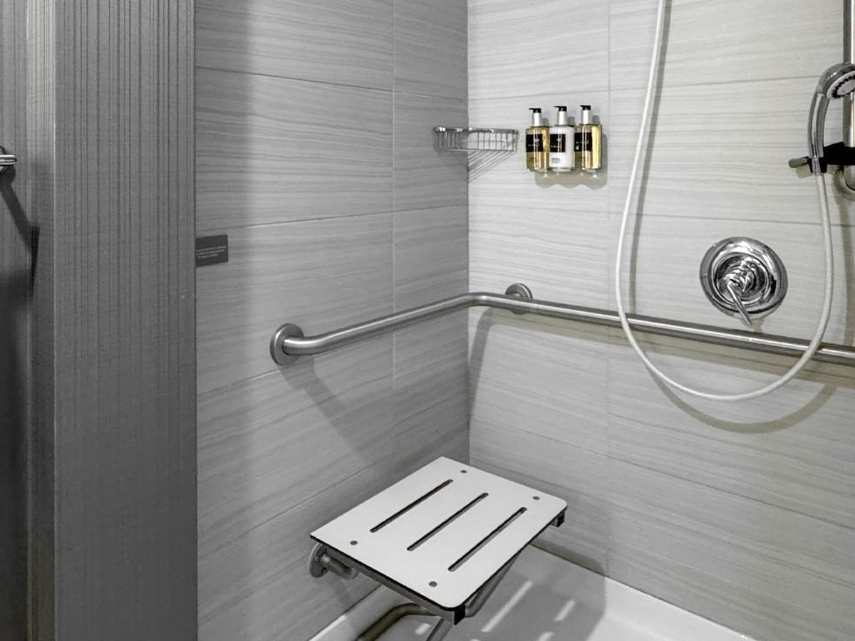 A bathroom with a shower, grab bars, and a shower seat.