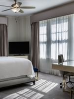 Sleek glass desk by a white bed under a ceiling fan in a bright, modern room in Presidential Suite at Warwick Melrose Dallas