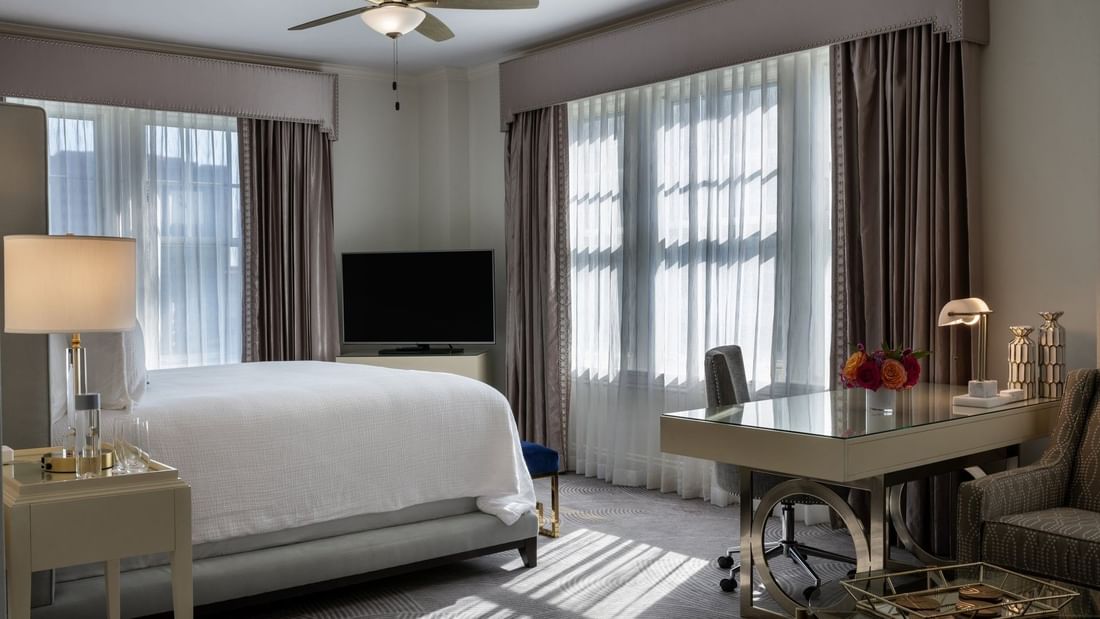 Sleek glass desk by a white bed under a ceiling fan in a bright, modern room in Presidential Suite at Warwick Melrose Dallas