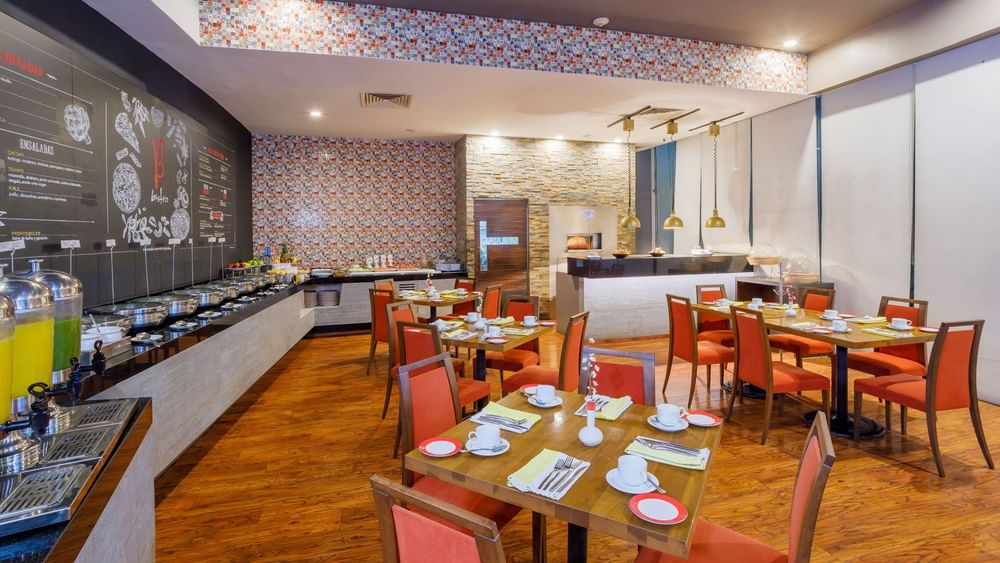 Modern buffet area in Bistro restaurant with orange chairs, wooden floors, and a colorful mosaic wall at Camino Real Pachuca