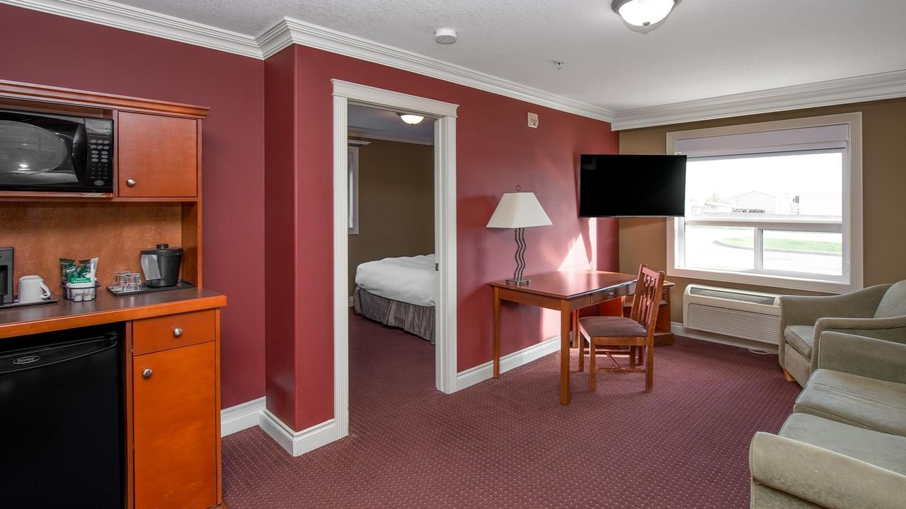 Suite with burgundy walls, kitchenette, wooden desk, beige sofa, and bedroom view at Coast Edson Hotel