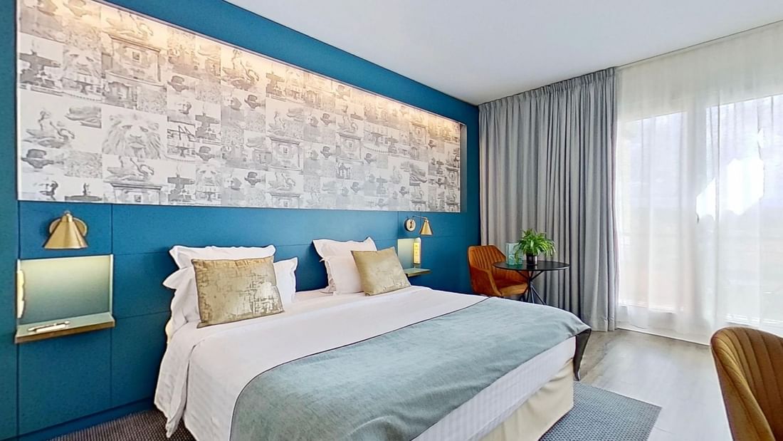 A bedroom with blue walls, a bed, nightstands, a chair, and a window with curtains.