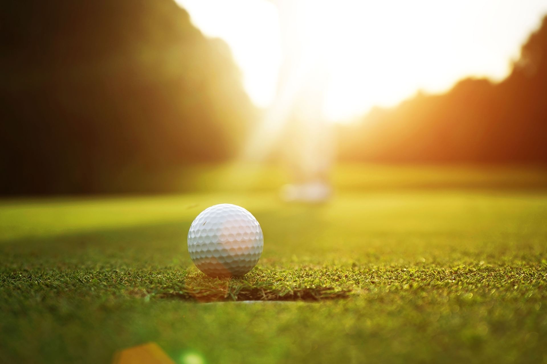 Golf ball resting by the hole on a putting green, under a golden sunset glow near Mountain View Grand Resort & Spa
