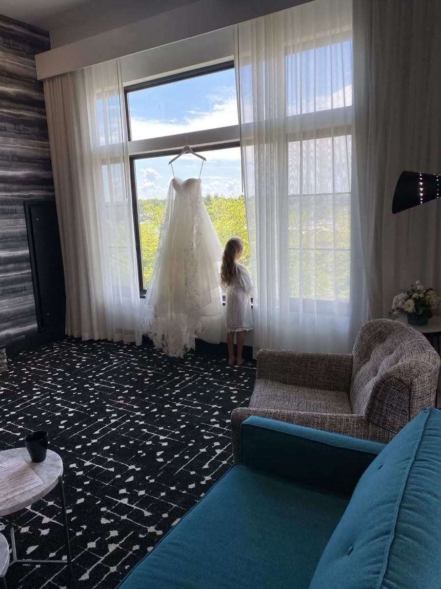 Girl standing by a Bride's wedding dress hanging by the window in a Suite at The Earl