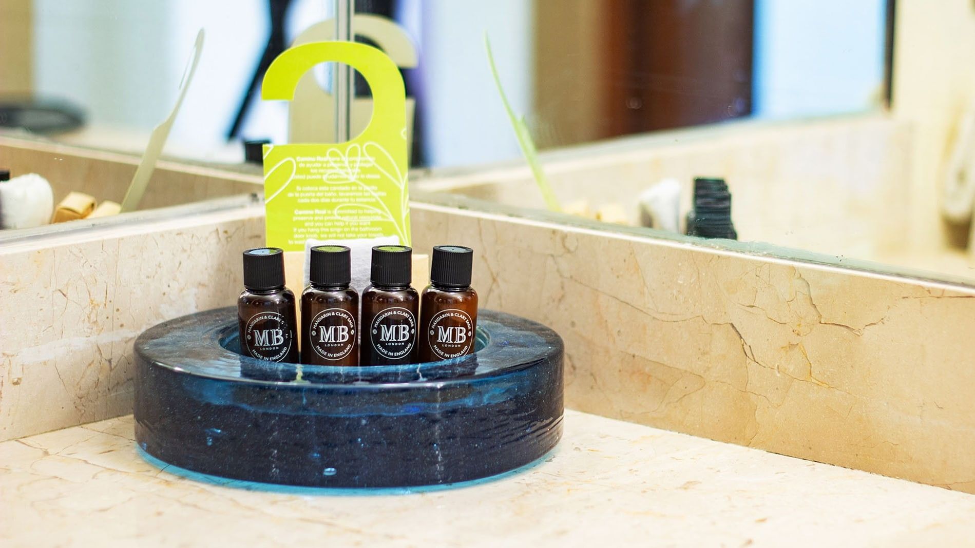 Cuatro frascos de aceites esenciales MB en un soporte circular azul en un baño.