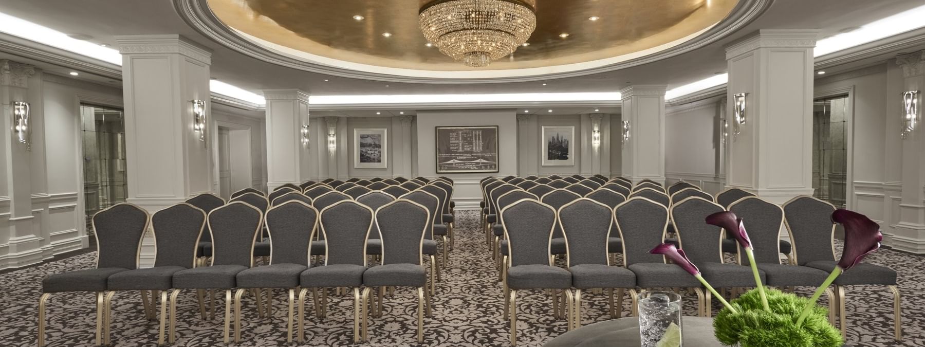 Elegant event hall arranged with theater seating facing a table with a microphone & glass of water at Warwick New York