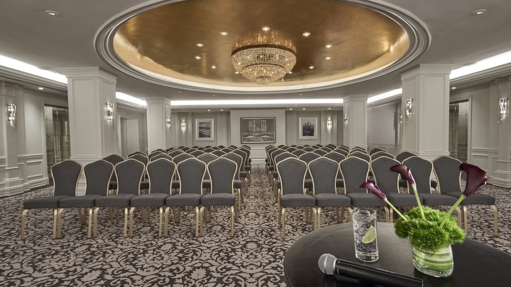 Elegant event hall arranged with theater seating facing a table with a microphone & glass of water at Warwick New York