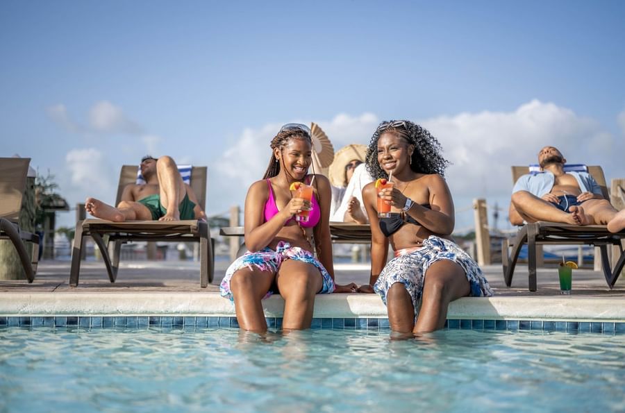 Smiling guests with tropical drinks by the pool under a clear blue sky at Warwick Paradise Island Bahamas