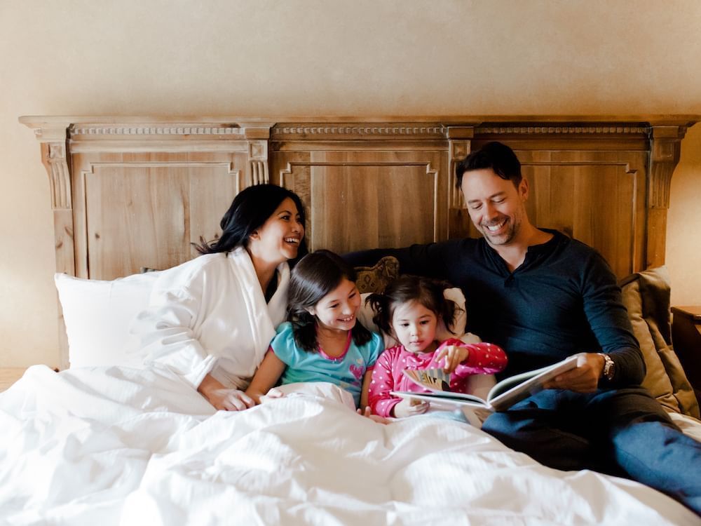 Mother and father reading a book to children in Chateaux guest room