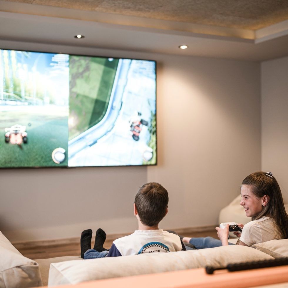 Children play racing game on large TV in living room at Falkensteiner Family Resort Sicily