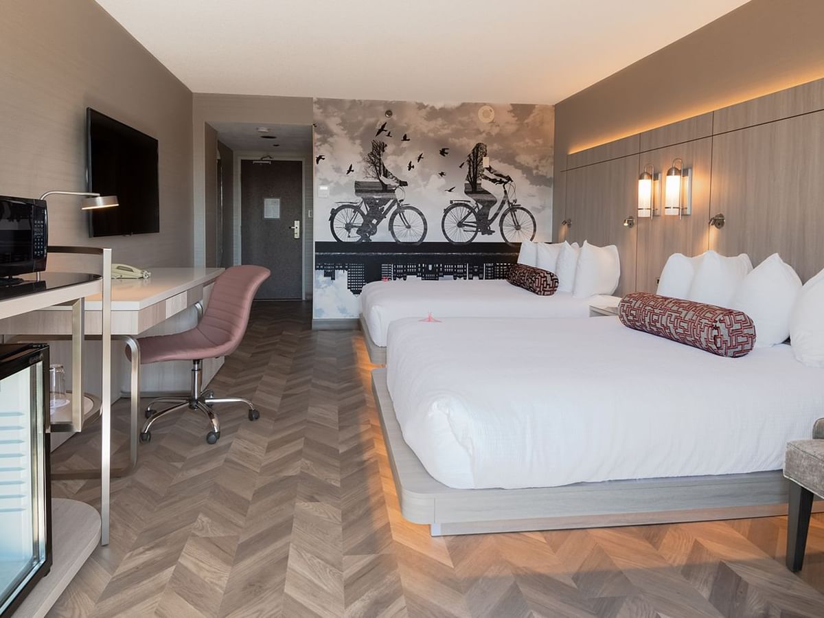 Hotel guestroom with two queen beds, mini fridge, microwave, work desk, chair, and TV