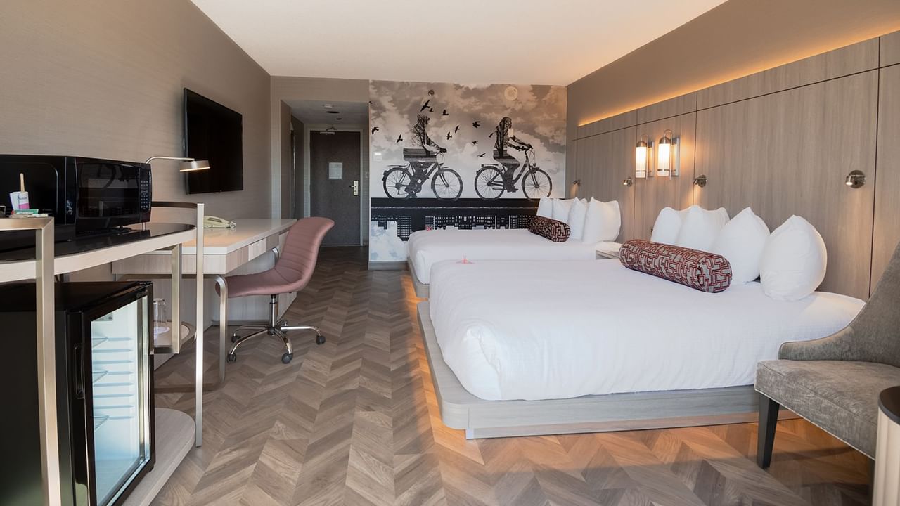 Hotel guestroom with two queen beds, mini fridge, microwave, work desk, chair, and TV