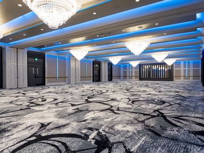 Carriage House Large, empty event hall with decorative carpet, crystal chandeliers, and blue lighting on the ceiling.