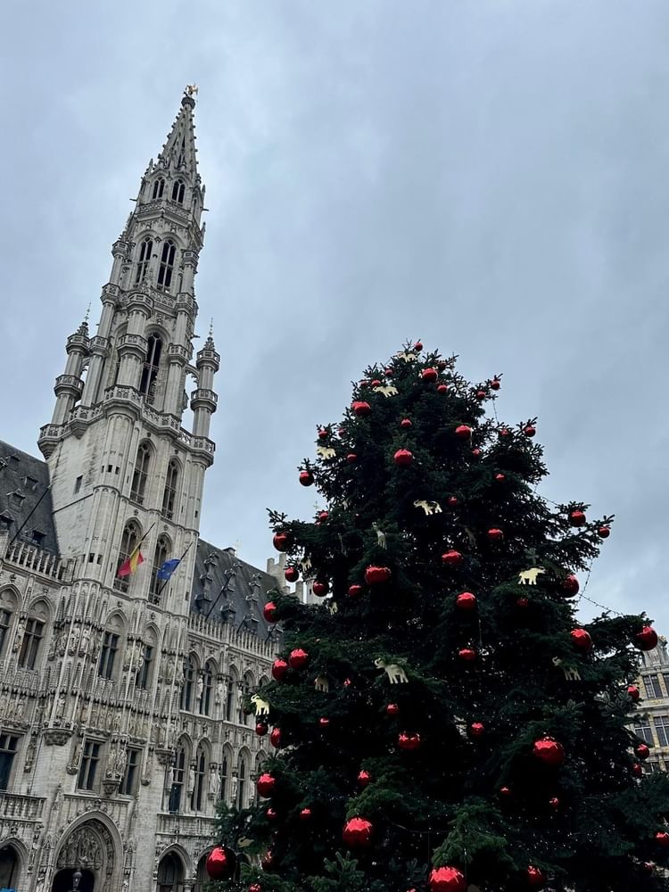 Tall Christmas tree with red ornaments sits by a gothic spire under a gray sky near Warwick Hotels & Resorts