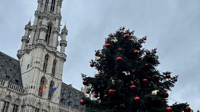 Tall Christmas tree with red ornaments sits by a gothic spire under a gray sky near Warwick Hotels & Resorts