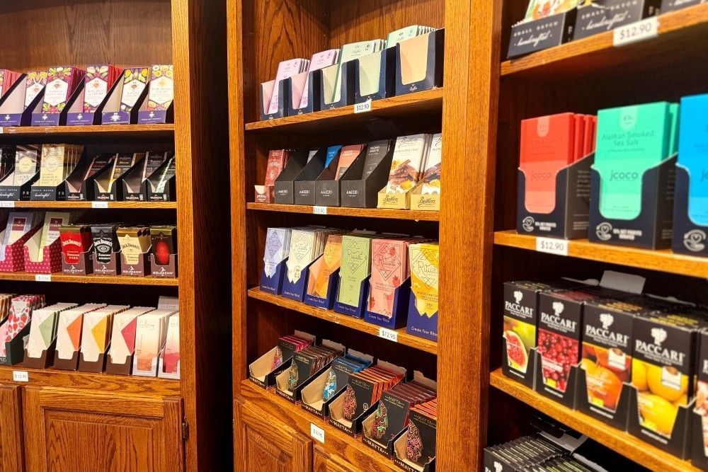 A close-up of wooden bookcases lined with displays of colorfully wrapped chocolate bars.
