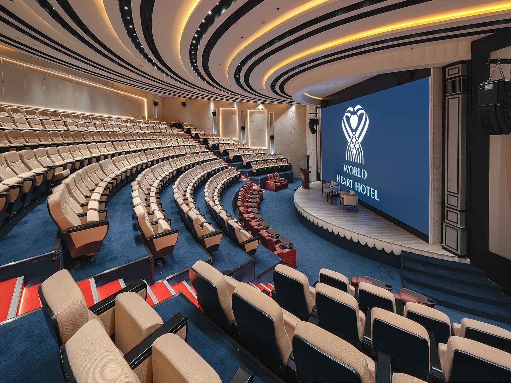 Large auditorium with rows of seats and a stage at World Heart Hotel.