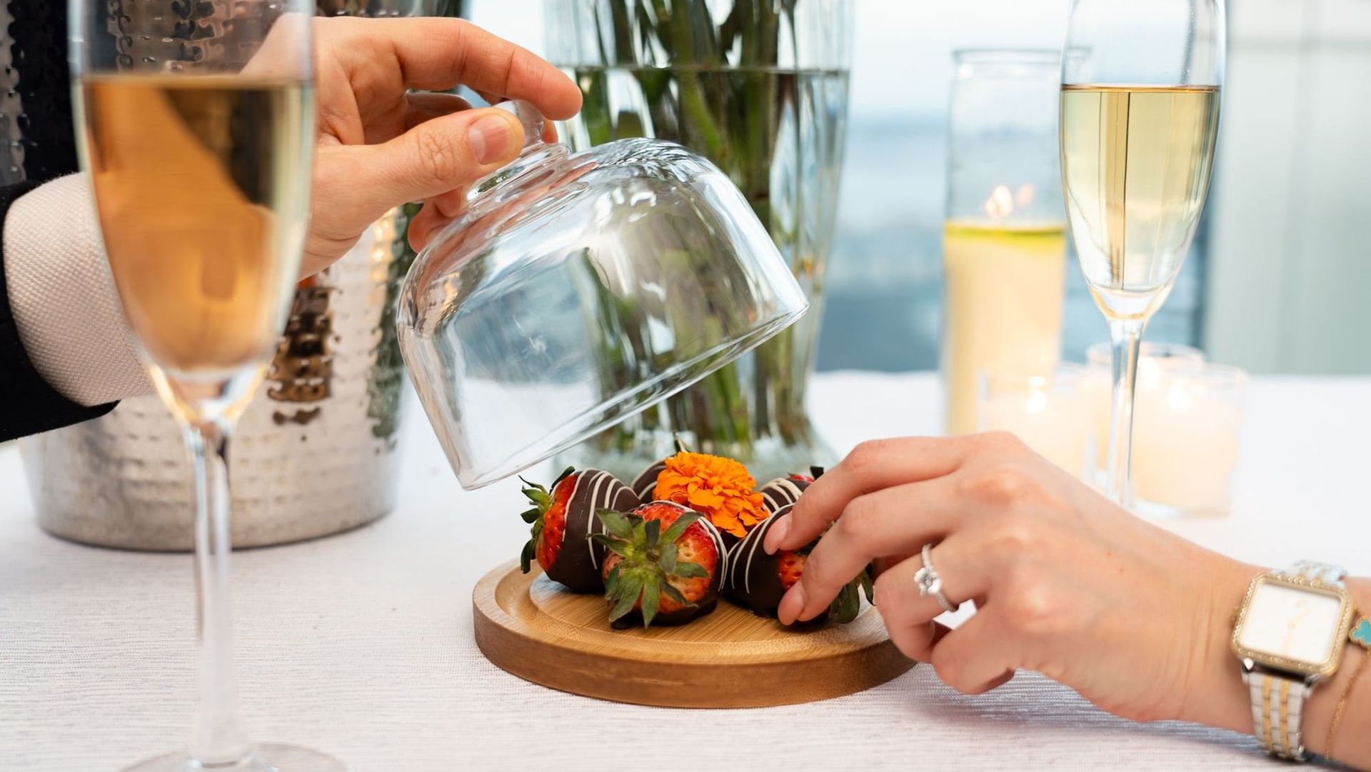 Chocolate-dipped strawberries on a wooden board, under a glass dome by champagne flutes and candles at Hotel X Toronto