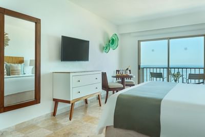 Interior view of a modern resort suite looking out to a sunny private balcony with ocean views.