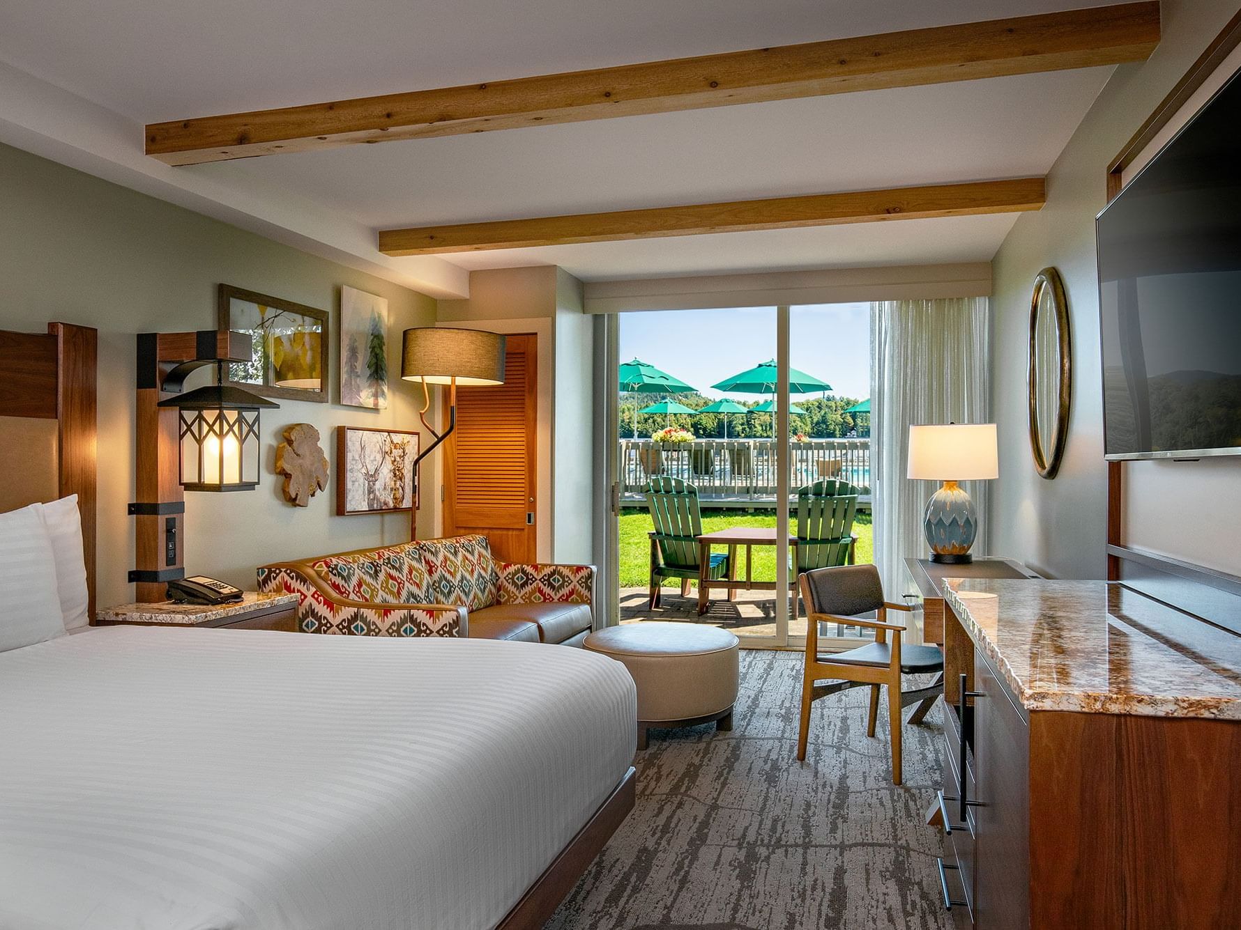 TV facing bed with a paterened sofa by the window and balcony area in Poolside King at High Peaks Resort