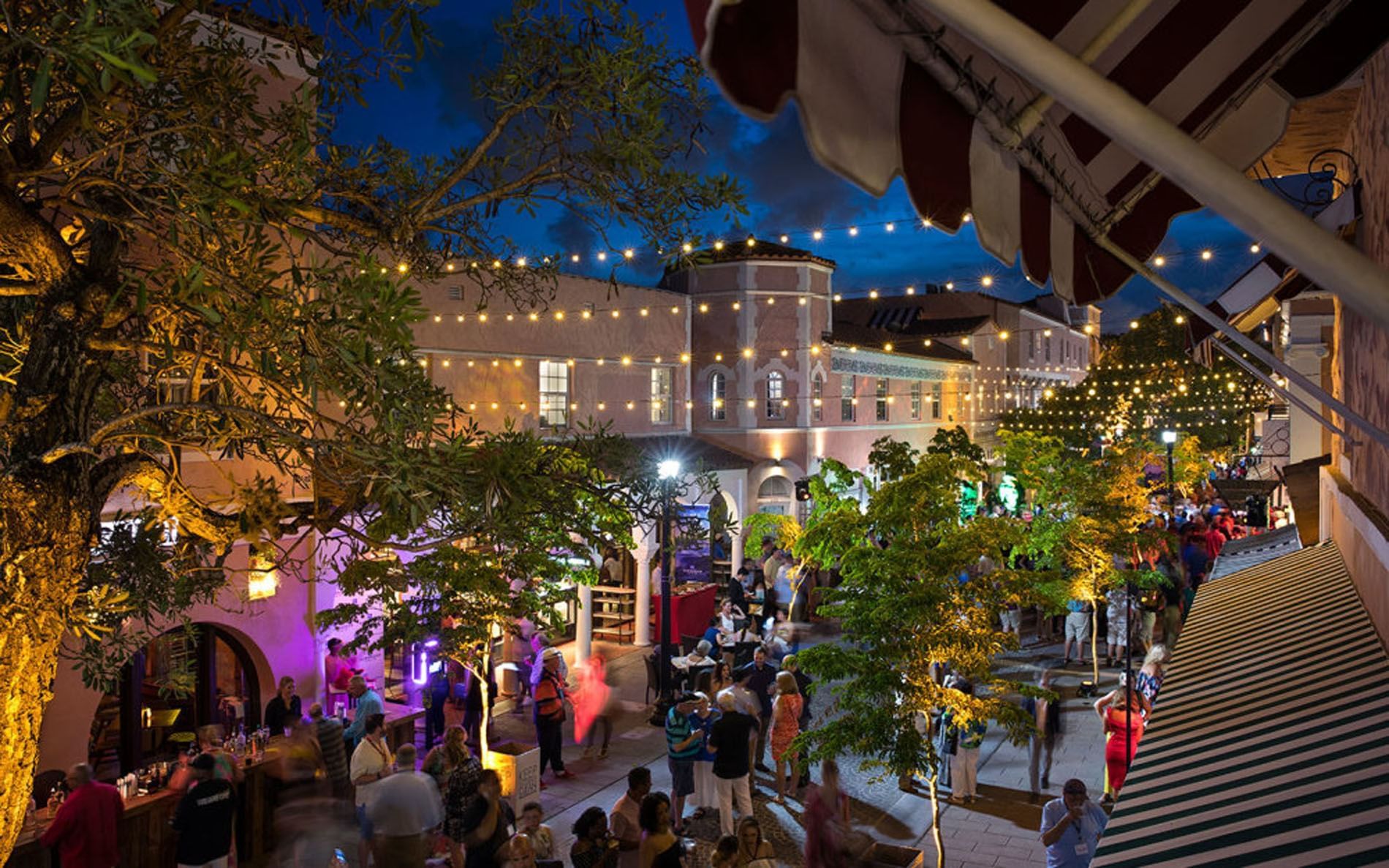 A courtyard with people, trees, and string lights at night.