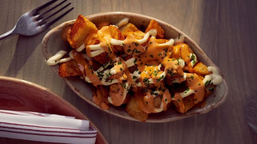 Crispy potatoes with spicy sauce & a bowl by a fork on a wooden table in In-Room Dining at Warwick San Francisco