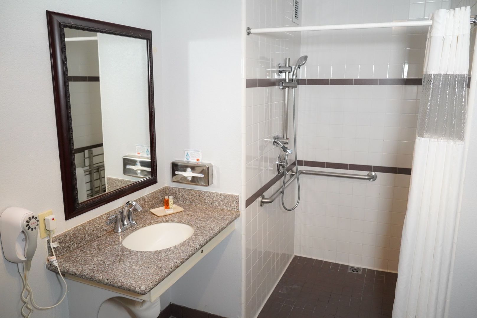 A clean and well-appointed bathroom with a granite countertop sink, large mirror, and a shower with grab bar and curtain.