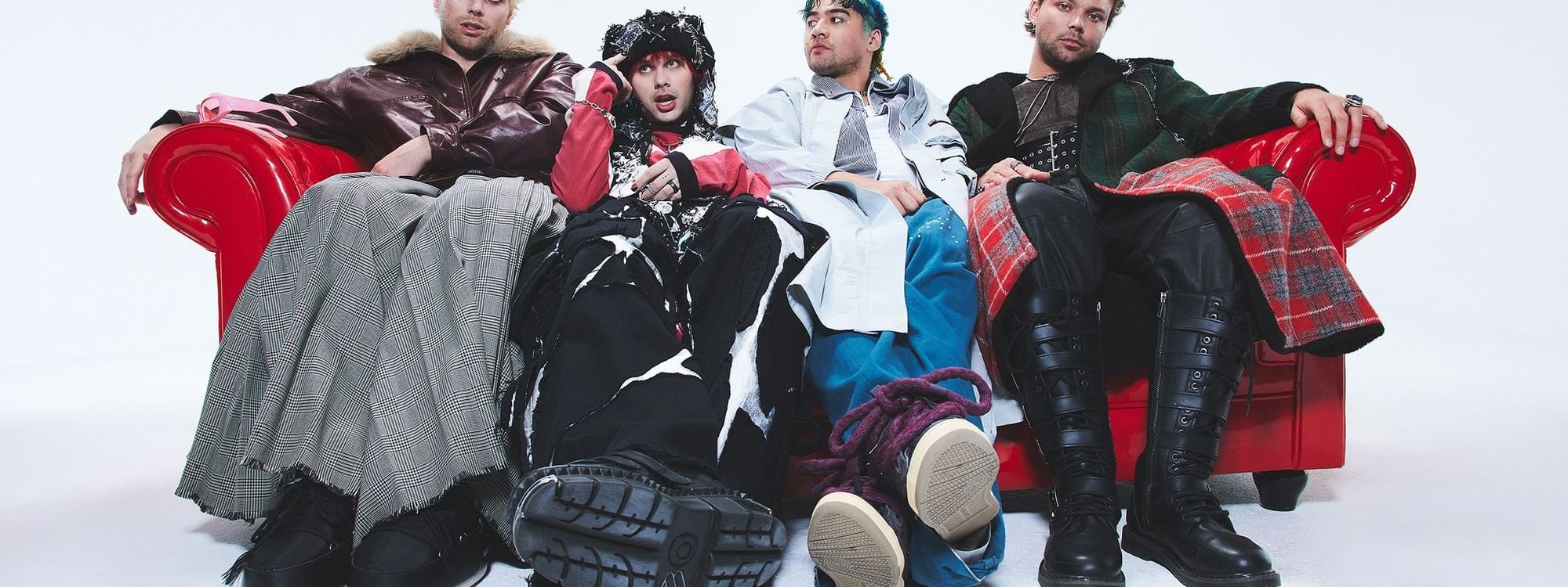 Four musicians from 5 Seconds of Summer seated on a red couch.
