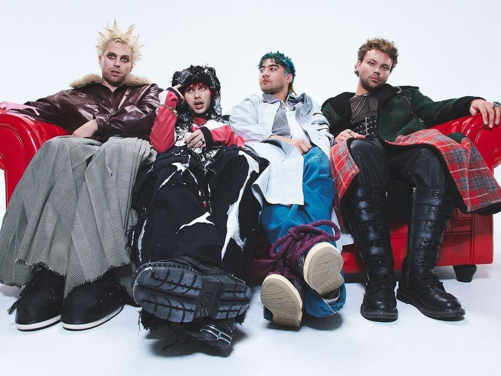 Four musicians seated on red couch promoting 5 Seconds of Summer – EVERYONE’S A STAR! World Tour.