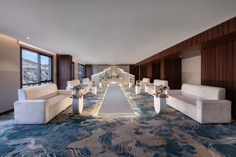White couches by side tables under a flat ceiling surrounding a white aisle runner in Amarige hall at Warwick Al Taif Hotel