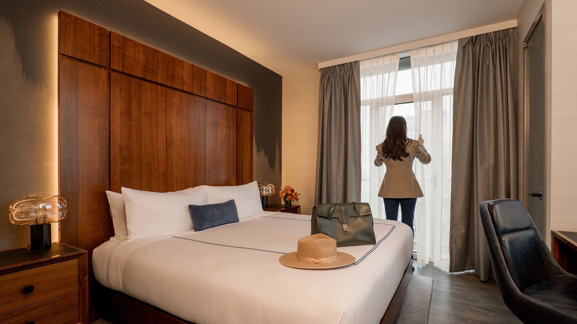 Two-Bedroom Gansevoort Suite with wood headboard, white bedding, and guest at window at Gansevoort Meatpacking NYC - NEW