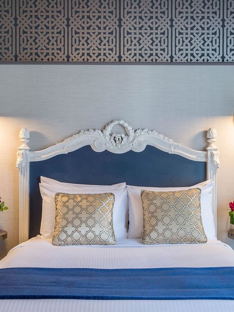 Floral vases on round tables by a bed under an ornate white headboard in Superior Queen Room at Warwick San Francisco