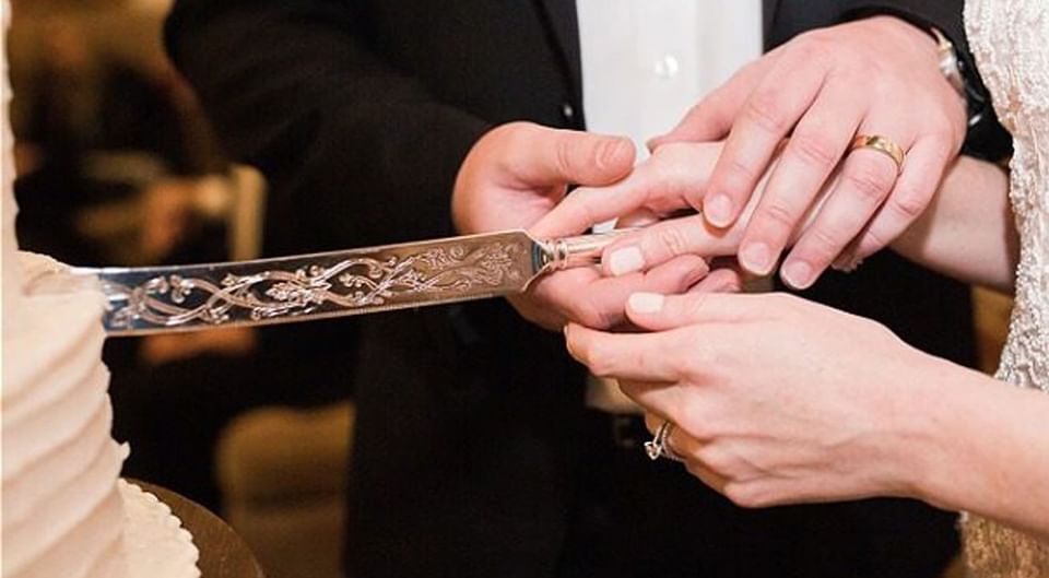 Close-up of wedded couple cutting the cake in Inn at the Crossroads