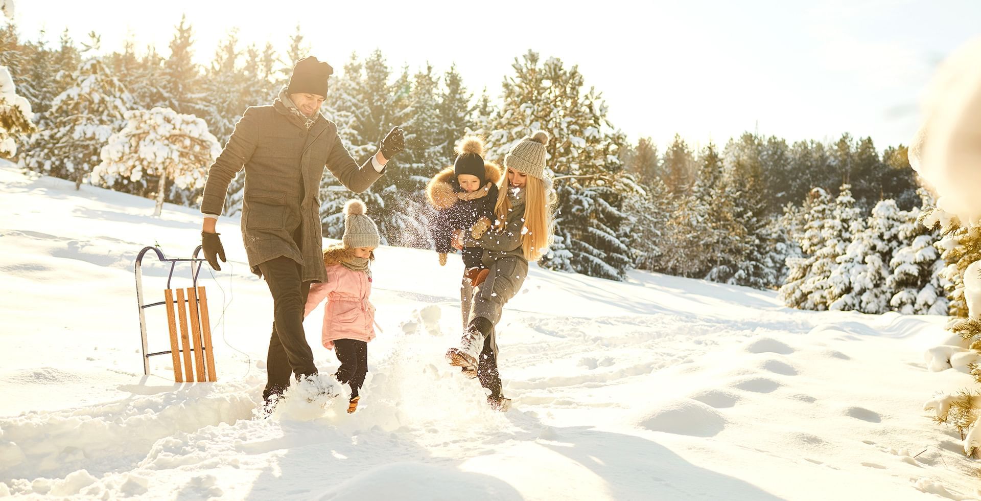 Family of three playing in the snow and Man holding a sled