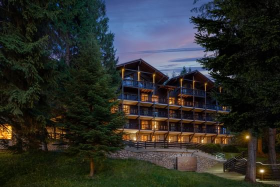 Exterior view of illuminated Ana Hotels Sport Poiana Brașov through trees