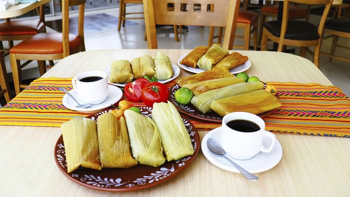Tamales mexicanos frescos en platos de cerámica estampados junto a café negro en La Pérgola de Araiza Palmira 