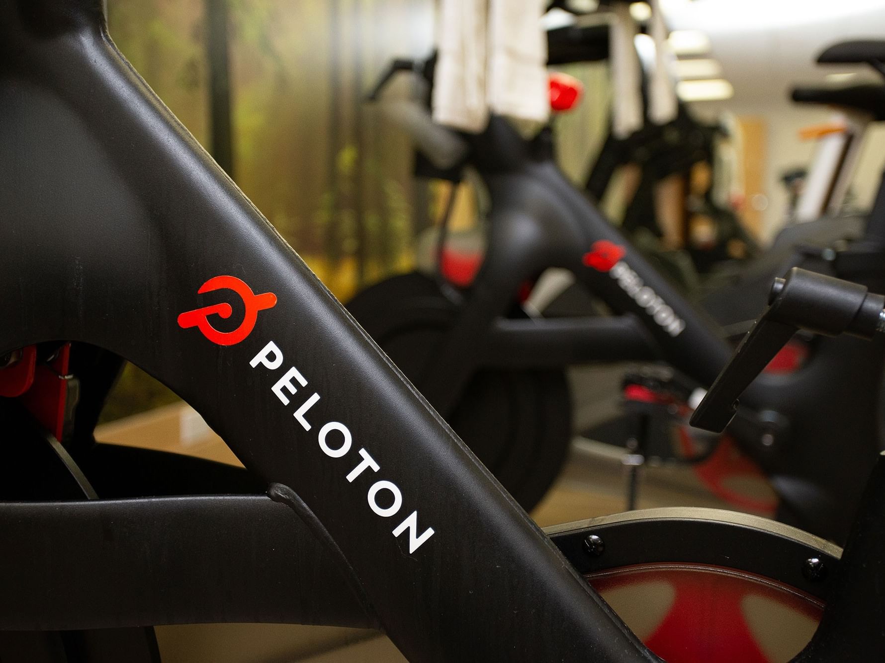 Peloton bike in a gym with other bikes, showing the logo and handlebars.