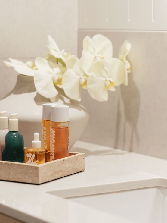 Wellness Suite Twin at Elysium Manly in a stone tray by a white orchid vase under a mirror beside the sink and a black tap