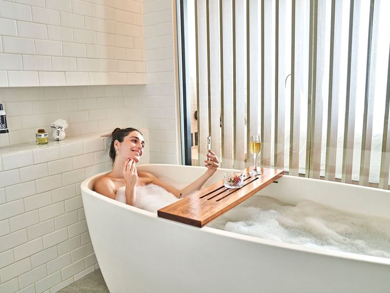 Lady enjoying a bubble bath & wine at IOH Freestyle Hotels