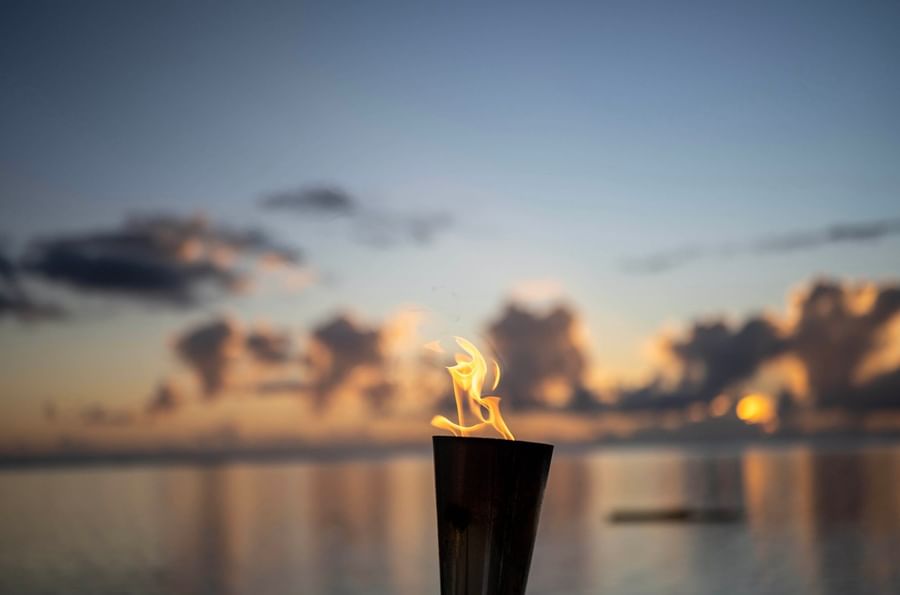 Bright torch flame in a dark cup by a calm sea under a soft sunset at Warwick Fiji Resort and Spa
