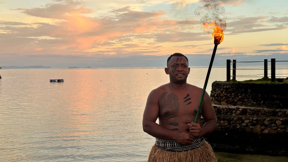 Man with torch at sunset by the ocean at Warwick Fiji Resort and Spa, Korolevu.