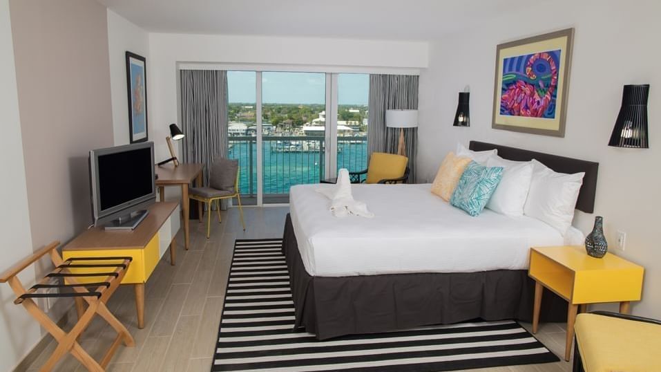 Plush bed by a yellow nightstand under a colorful painting in Deluxe Harbour Balcony King at Warwick Paradise Island Bahamas